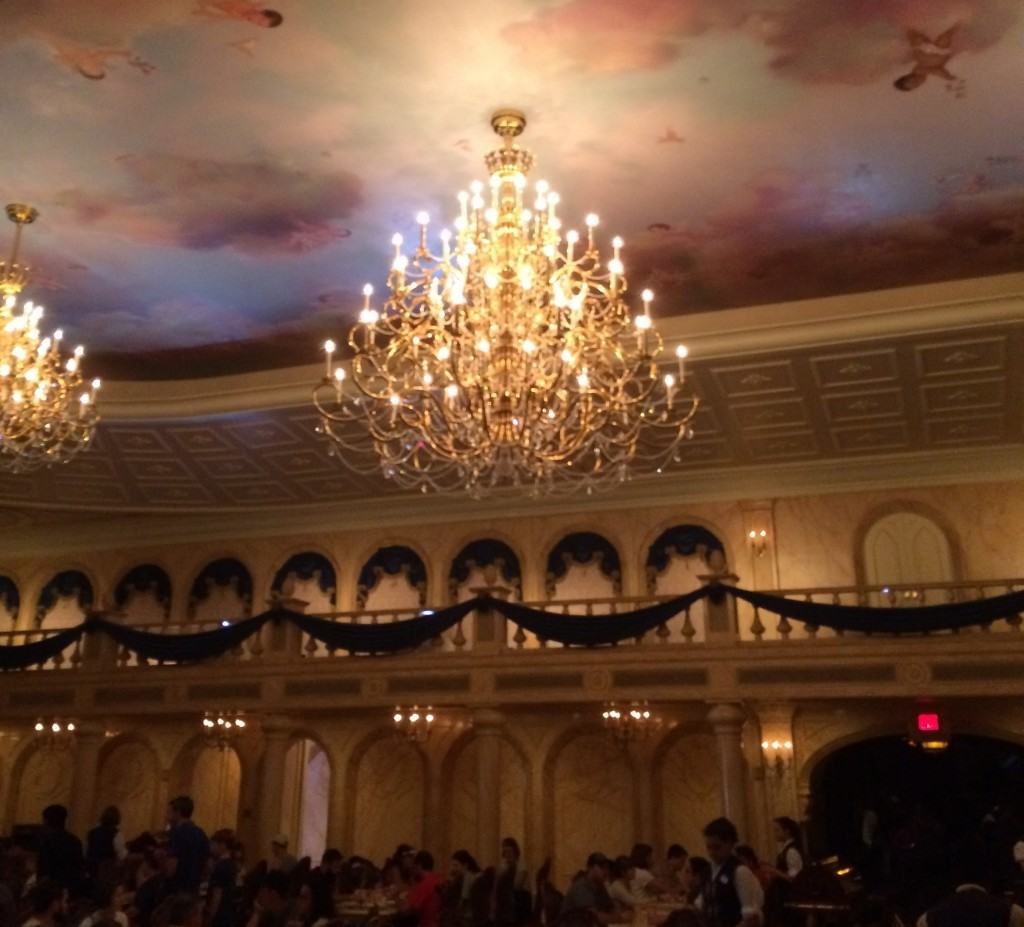 Be Our Guest's Main Dining Room with all the seats filled. Large chanderliers hang from the cieling along with a heavenly mural.