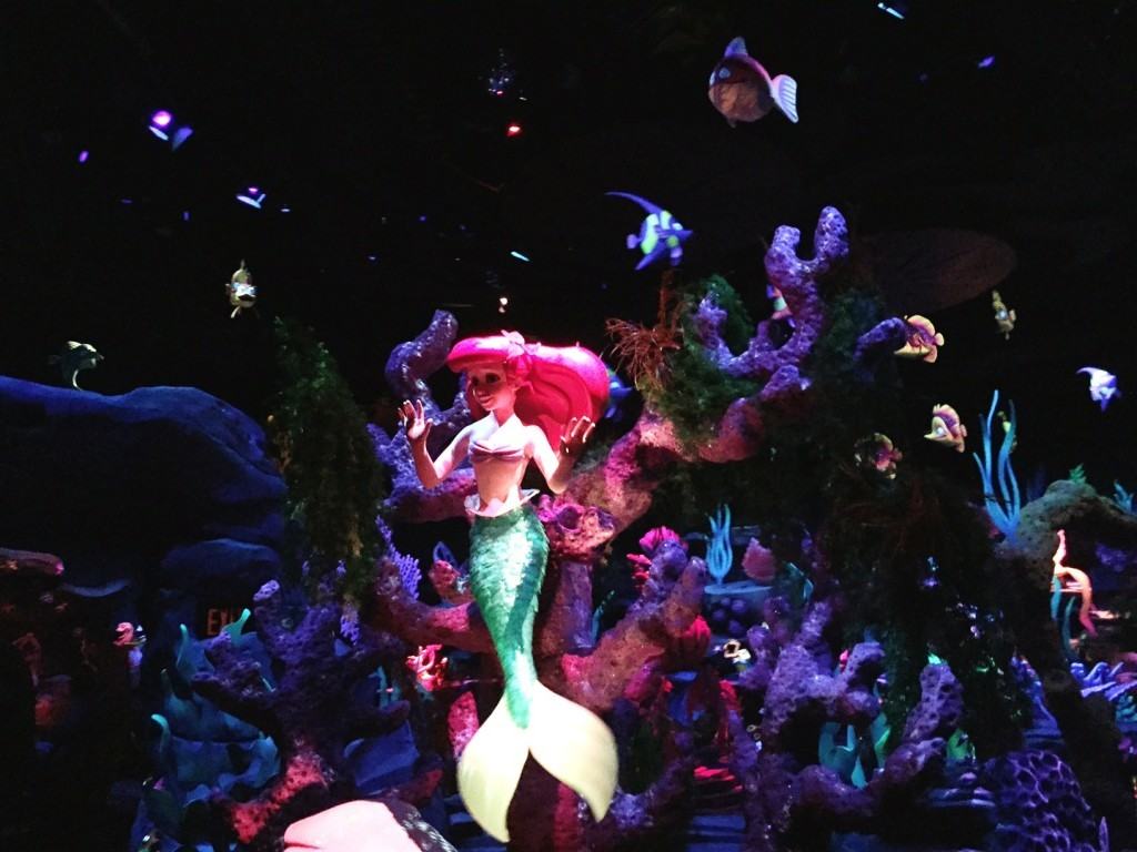 Ariel in the Little Mermaid Ride posing in front of a large colorful coral reef.