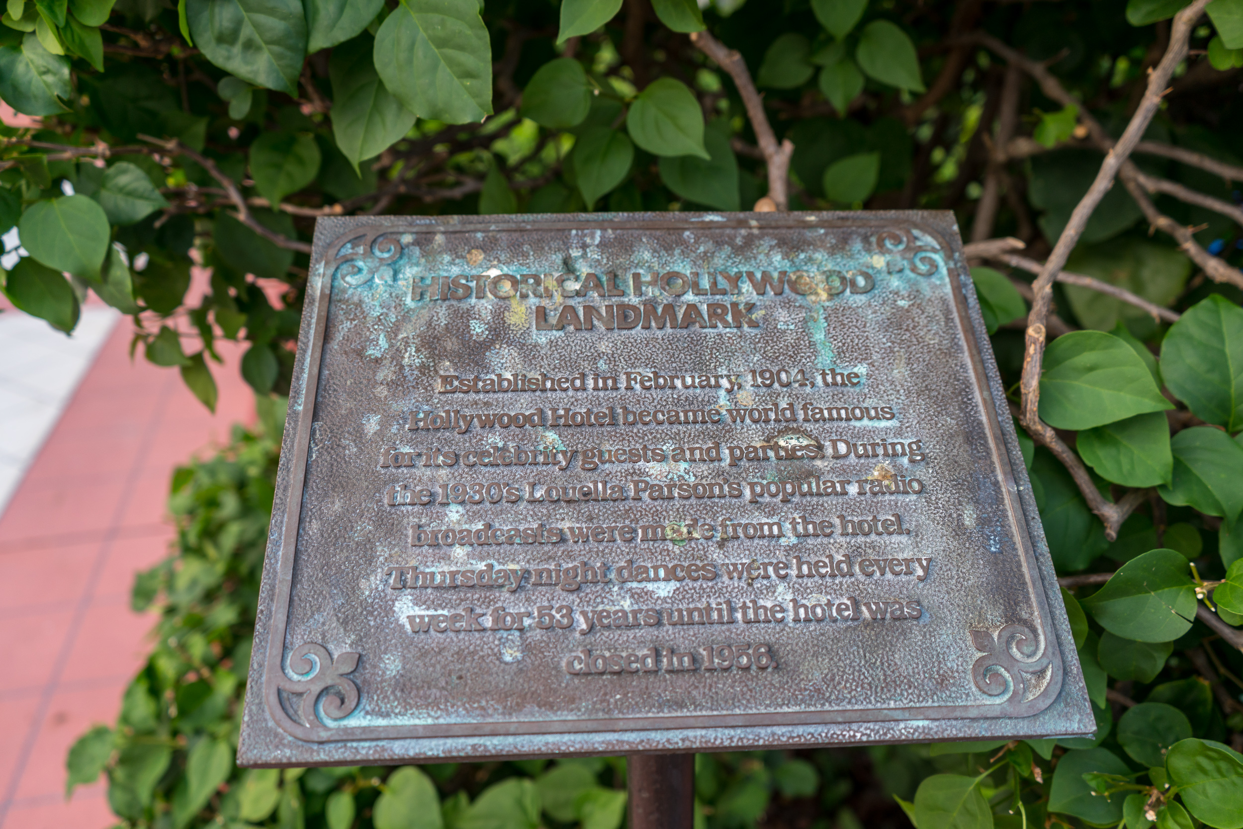 A plaque reads: "Historical Hollywood Landmark - established in February, 1904, the Hollywood Hotel became world famous for its celebrity guests and parties. During the 1930's Louella Parsons popular radio broadcasts were made from the hotel. Thursday night dances were held every week for 53 years until the hotel was closed in 1956."