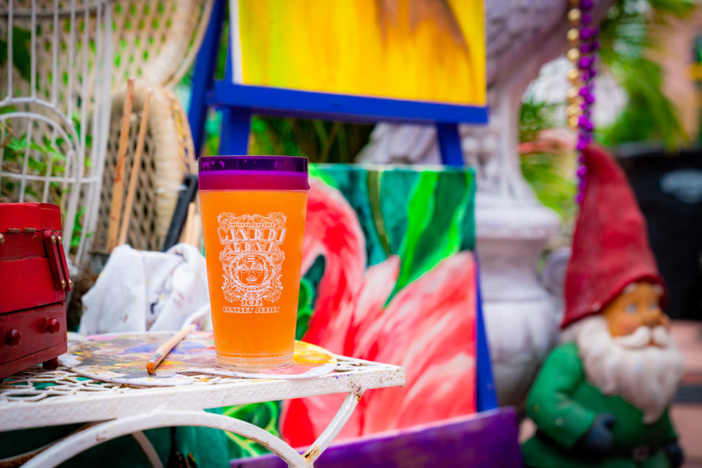 Cup with an orange body and purple lip with a white decal image that includes the words "Universal Orlando's Mardi Gras 2022 Concert Series". 