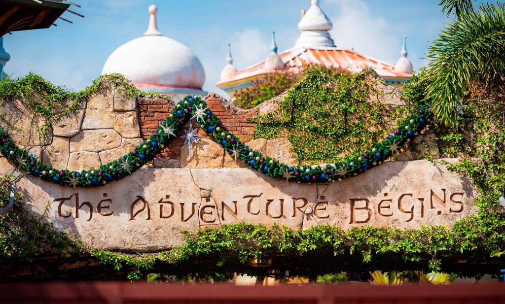 "The Adventure Begins" engraved sign at Islands of Adventure and decorated with seasonal garland