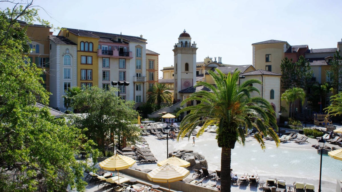 Italian-themed buildings and palm trees set the scene for the zero entry Beach pool, where guests relax in pool lounge chairs.