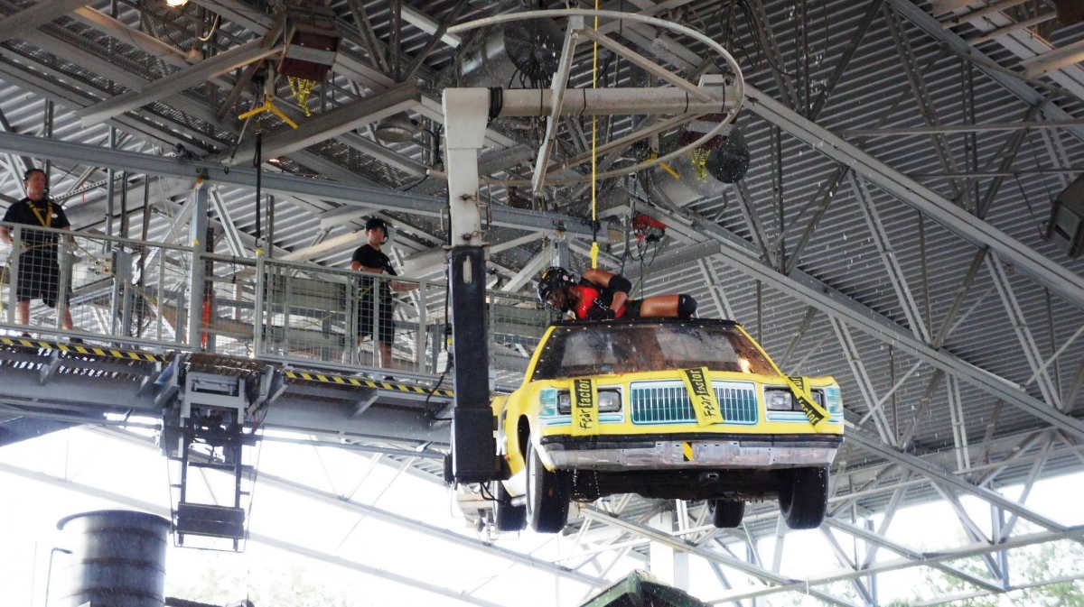 A contestant climbs into a yellow convertible car, suspended in the air